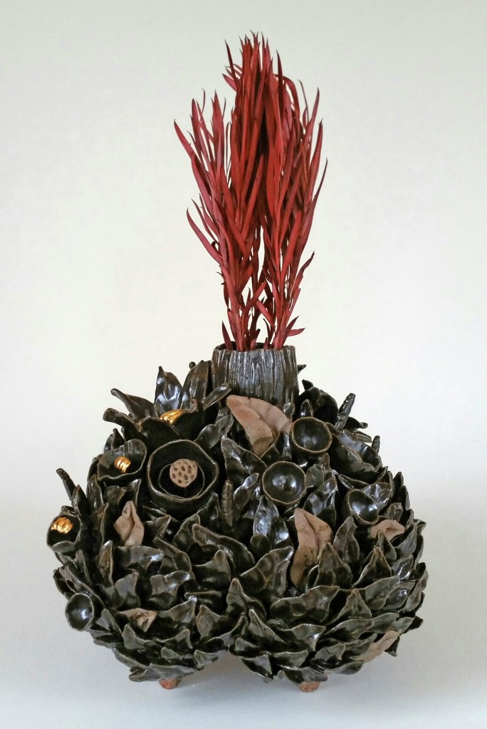 Ceramic sculpture vase with floral buds and red firey foliage in it.